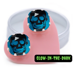 A pair of Glow in the dark earrings, featuring skulls on a Bright Aqua background, carded on a pink heart.